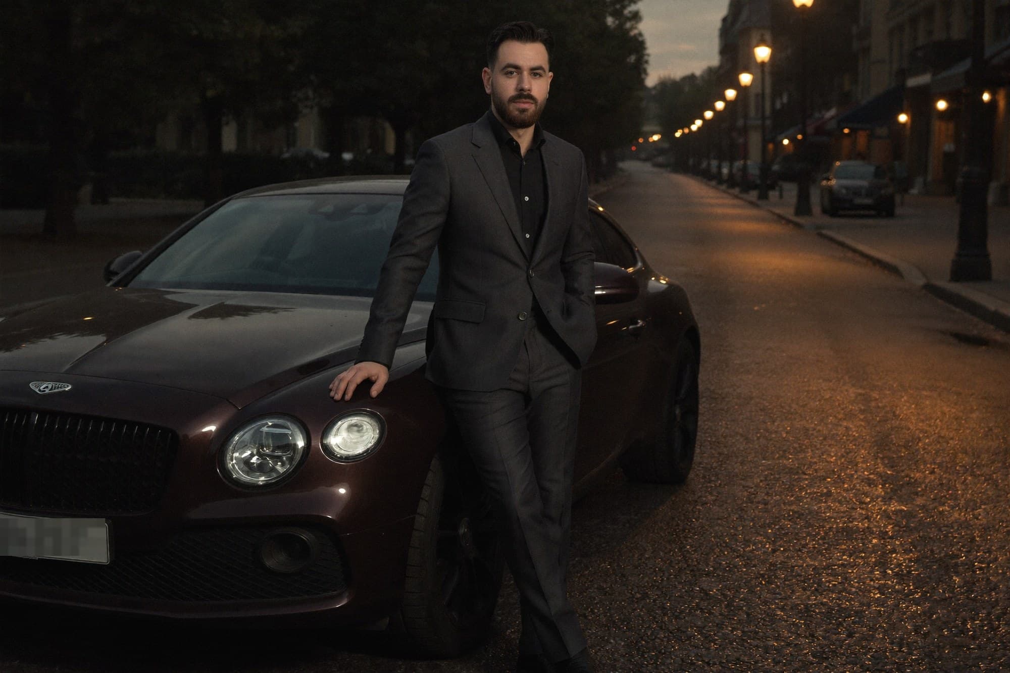 Chauffeur in a suit beside a dark car on an evening street