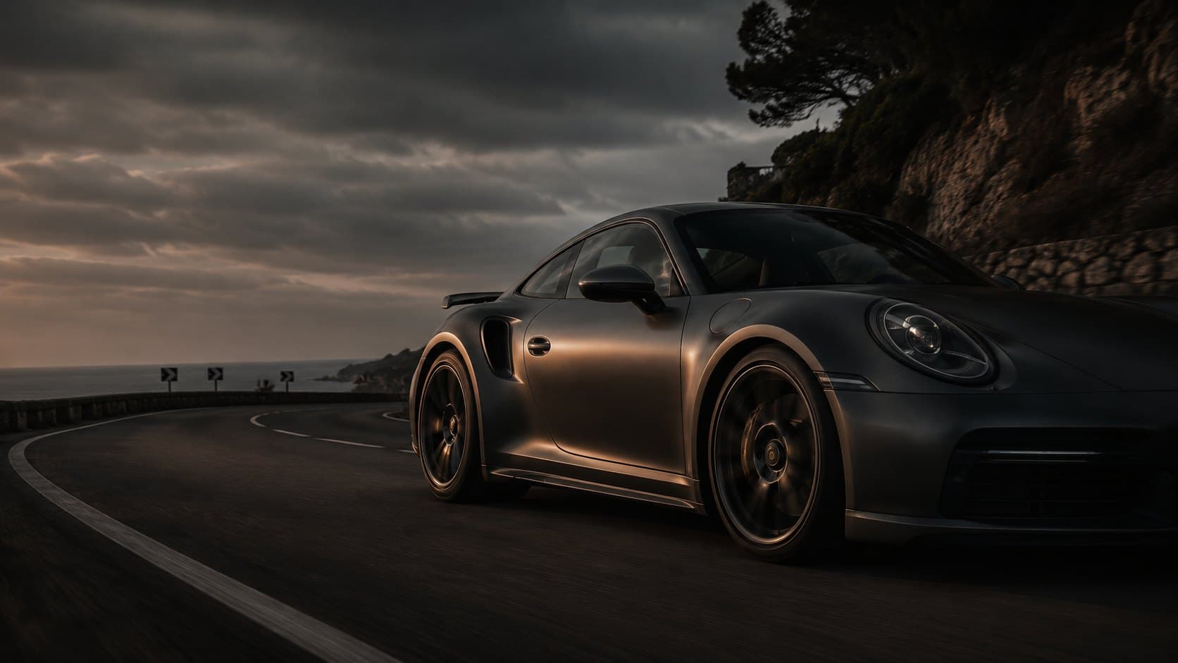 Donkere Porsche 911 Turbo op een Zuid-Europese kustweg in de schemering