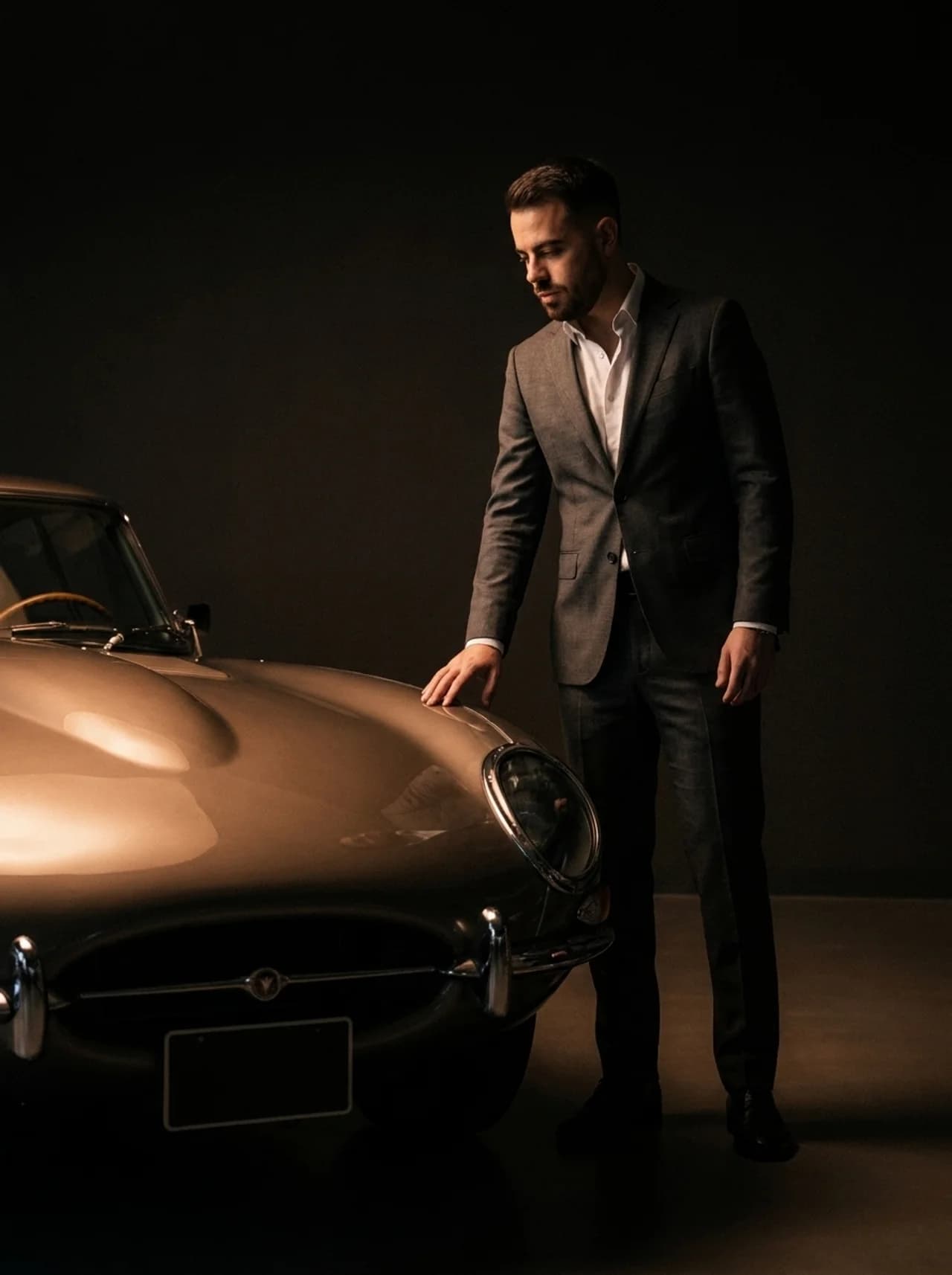 Elias in pak naast een klassieke Jaguar E-Type in een studio — car sourcing en aankoopbegeleiding