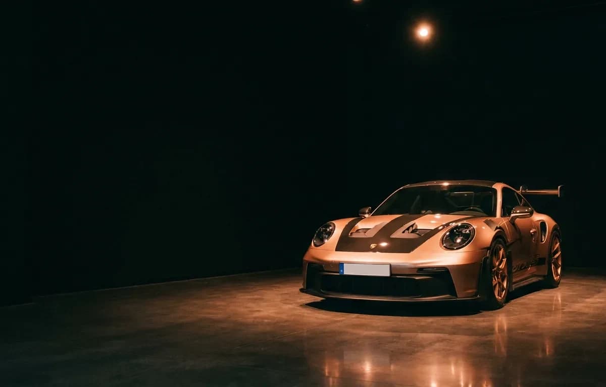 Koperkleurige Porsche 911 GT3 RS onder een spotlight in een donkere showroom